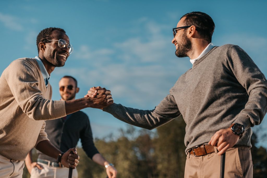 Happy Stylish Multicultural Friends Shaking Hands While Playing Golf on Golf Course